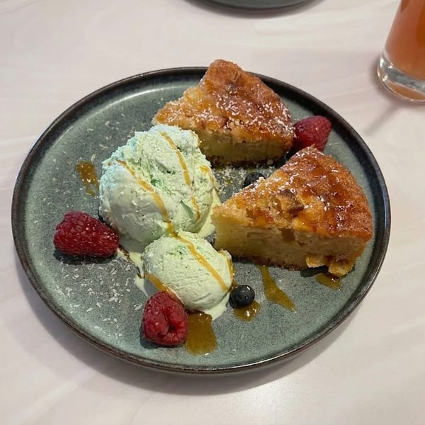 Two slices of cake with three scoops of green ice cream, raspberries, and blueberries on a plate.