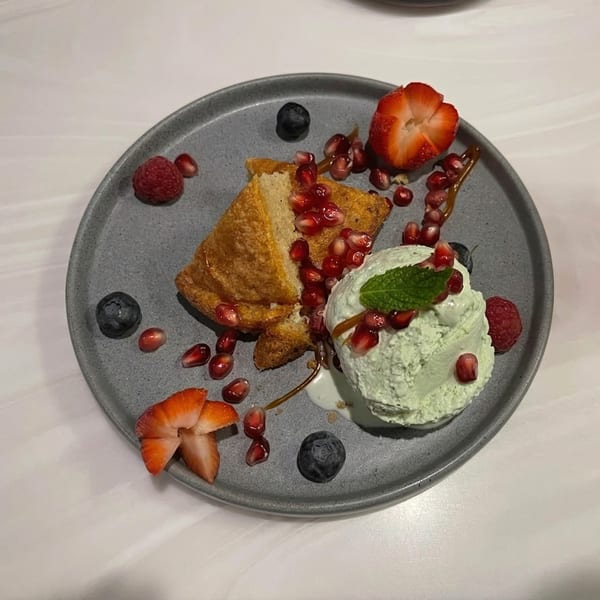 A dessert plate with cake, green ice cream, pomegranate seeds, strawberries, raspberries, and blueberries.