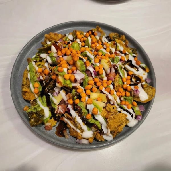 A plate of colorful Indian chaat, topped with sauces, onions, and crispy chickpea balls.