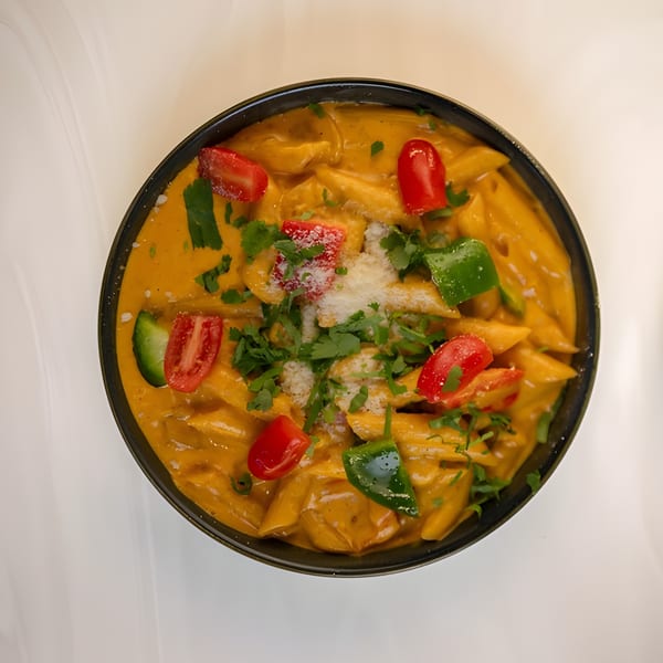 Penne pasta in a creamy orange sauce, topped with cherry tomatoes, green peppers, cilantro, and cheese.
