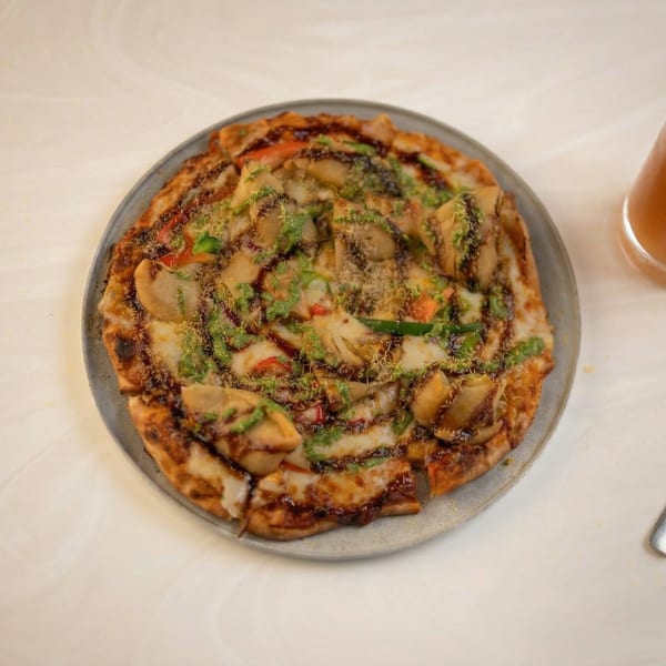 A round pizza with mushrooms, green and red peppers, and a dark sauce drizzle.