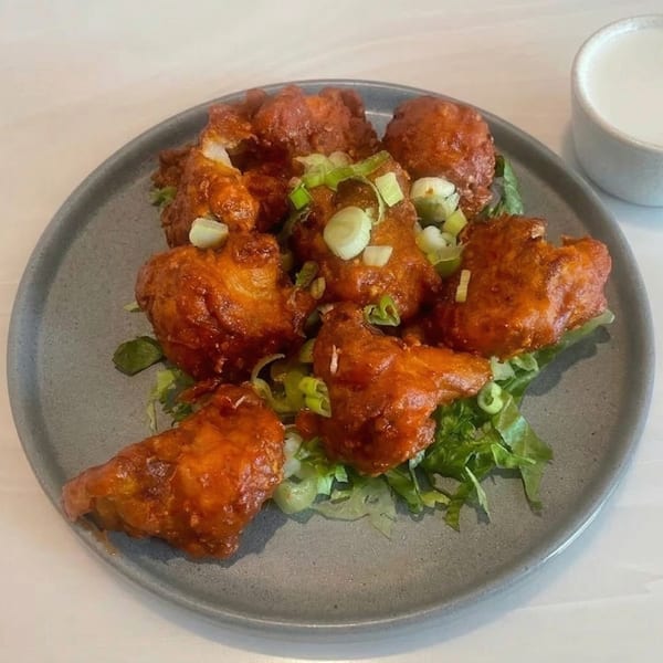 Spicy orange cauliflower bites on a bed of lettuce, garnished with chopped green onions.